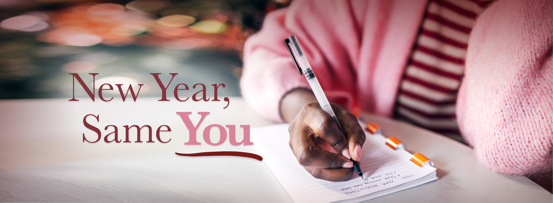 Photo of a woman in a pink sweater making resolutions in a notebook